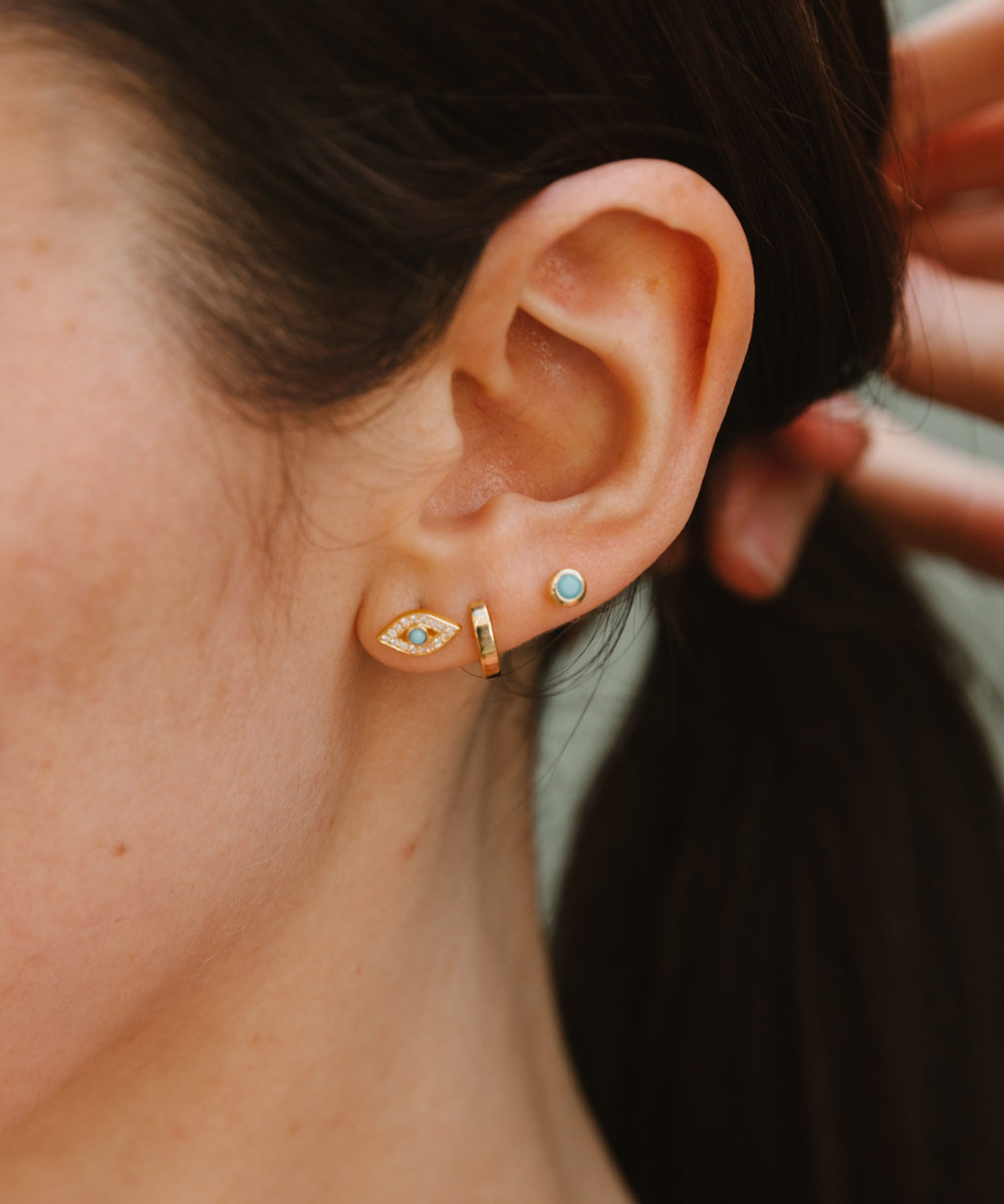 Model wearing the Tiny Biography Evil Eye Stud Earrings in Yellow Gold Vermeil styled with yellow gold vermeil stud and hoop earrings by Astley Clarke | The Astley Clarke Blog