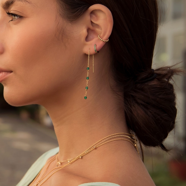 earring stack with green gemstone drop earrings, gold ear cuff and solid yellow gold huggie hoop earring with emeralds