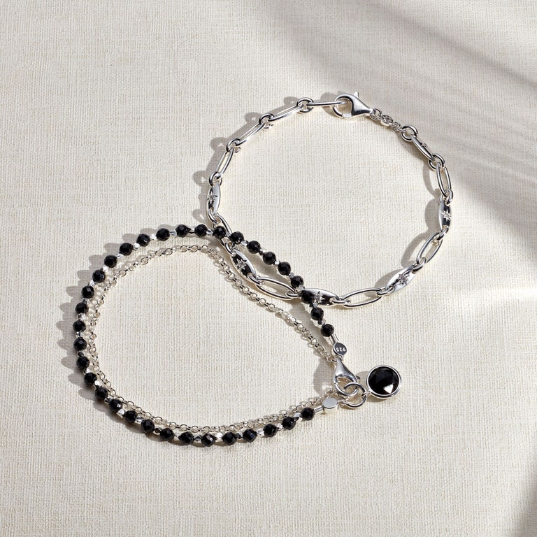 still life image of silver chain bracelet and black onyx charm bracelet
