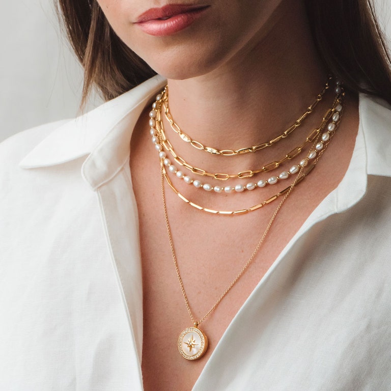 gold necklace stack with pearl choker and mother of pearl locket necklace