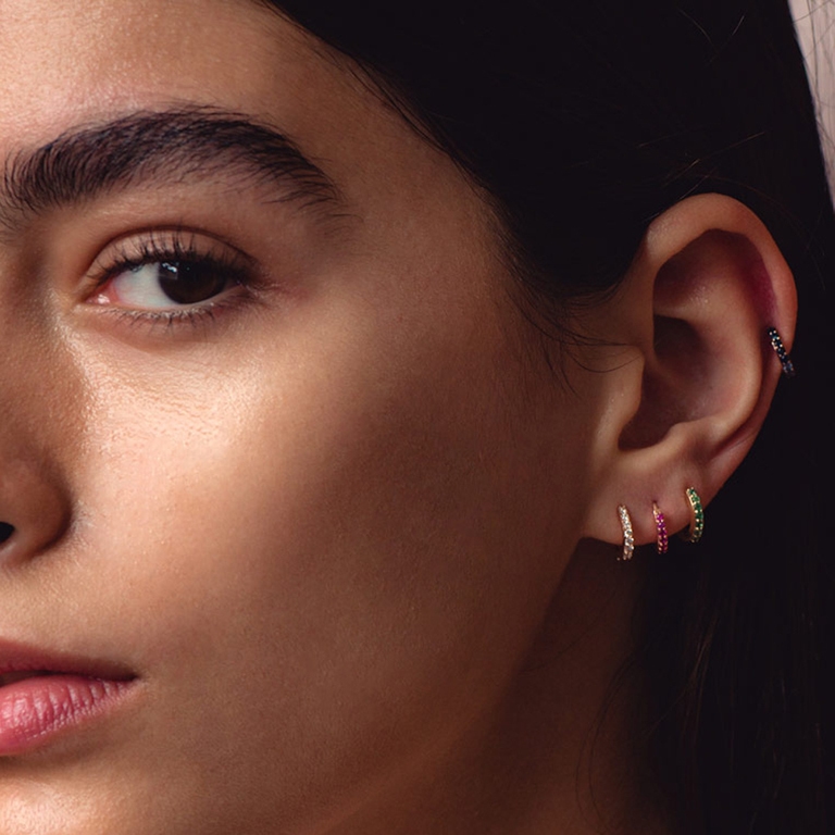 earring stack of solid gold huggie hoop earrings with diamond earrings, sapphire earrings and emerald earrings